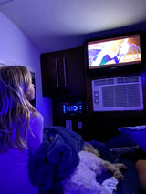 Relaxing evening inside an RV rental. A girl and a dog watch TV in the cozy, blue-lit interior.
