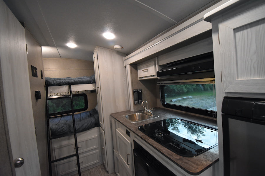 RV rental interior: bunk beds, full kitchenette with sink, stove, & fridge. Perfect for road trips & family comfort.