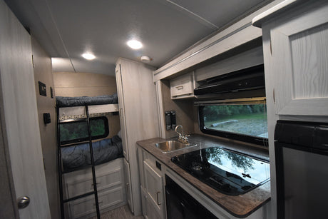 RV rental interior: bunk beds, full kitchenette with sink, stove, & fridge. Perfect for road trips & family comfort.