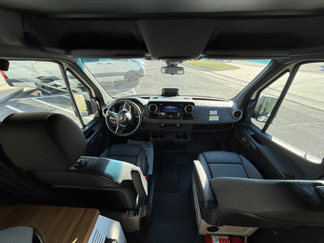 RV rental cockpit view: Mercedes dashboard, steering, infotainment screen, and front seats with a parking lot visible.
