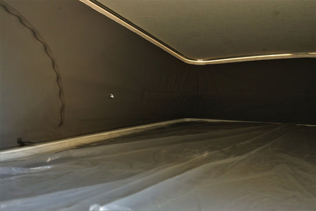 Interior of an RV rental pop-top. Shows the sleeping area with protective plastic covering, fabric walls, and roof lighting.