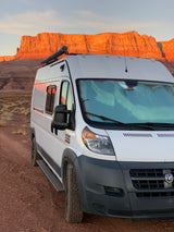 White Ram ProMaster RV rental parked in front of stunning red rock cliffs at sunset. Perfect for adventure!