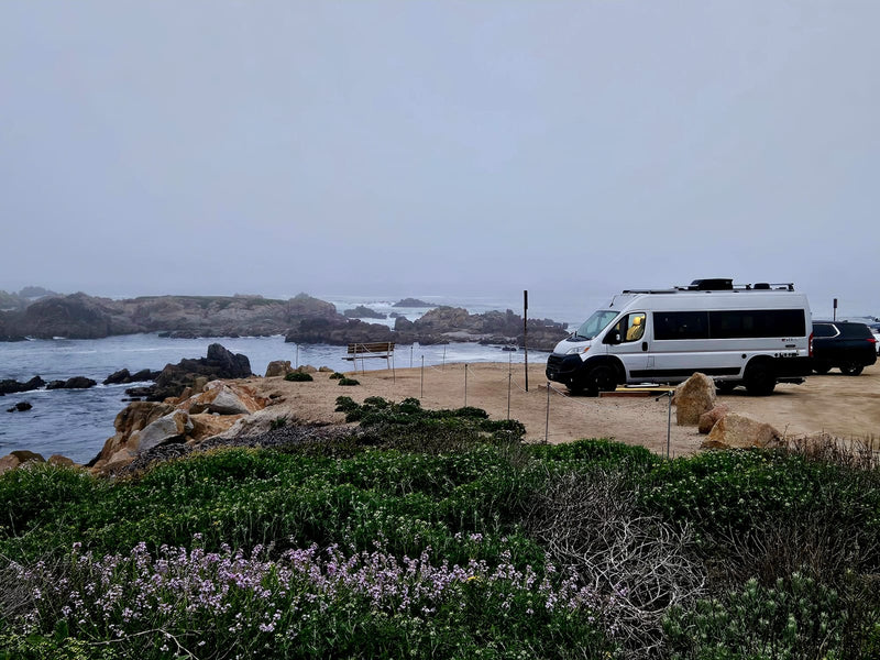  is parked outdoors with its warmly lit interior visible through the open side door.|Scenic RV rental camping: a white van on a sandy beach with chairs — photo 2