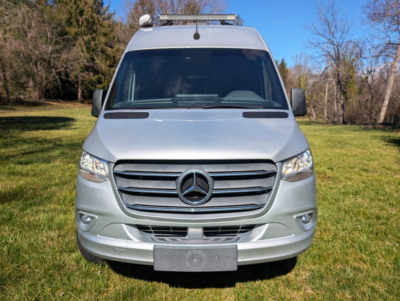 parked in a sunny grassy field.|Silver Mercedes Sprinter RV rental parked on vibrant green grass under a clear blue sky — photo 11