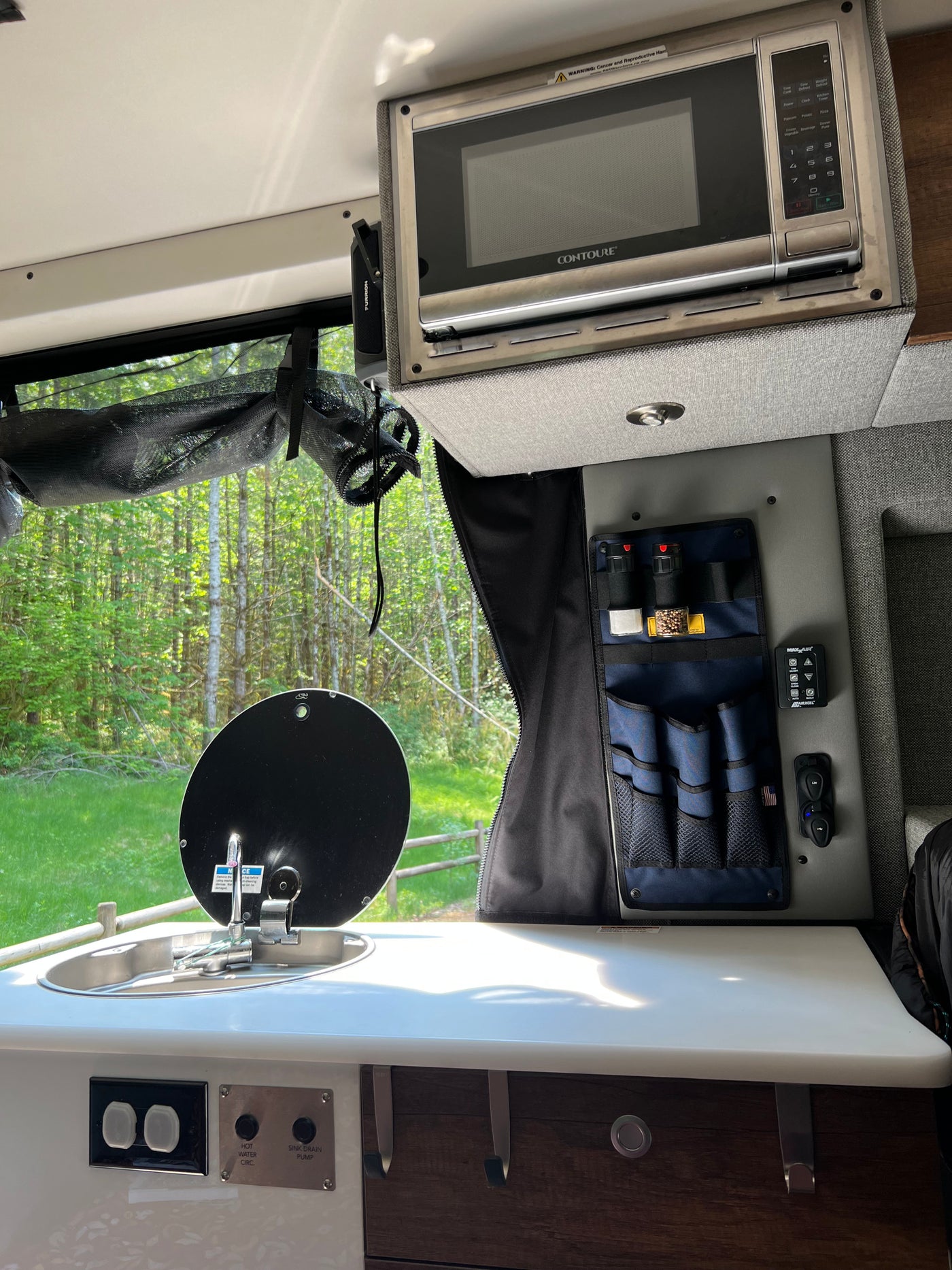 Inside an RV rental: Compact kitchen with a Contoure microwave, sink, & spice storage, enjoying nature views. — photo 18
