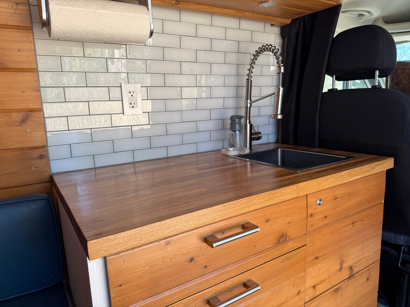 This RV rental features a modern kitchenette with a wood countertop, white subway tile backsplash, sink, and custom cabinetry. — photo 3