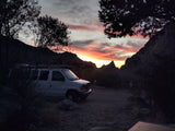 White RV rental van parked for a stunning mountain sunset, with vibrant orange and red skies.