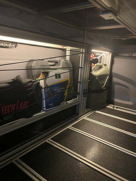 Organized RV rental interior: modular storage with camping gear, extension cord, jerry can, and LED lighting.
