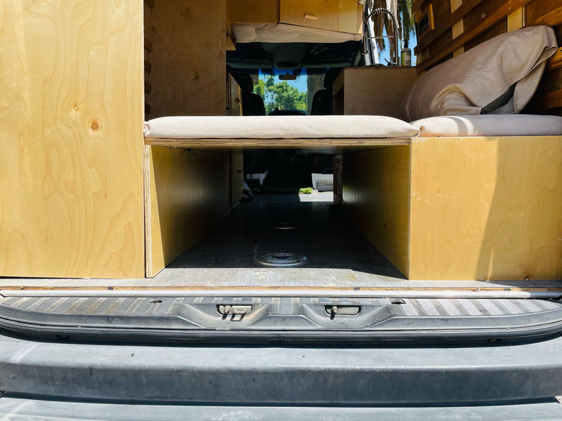 Inside an RV rental camper van: light wood storage, bed platform with cushions, looking forward through the windshield. — photo 15