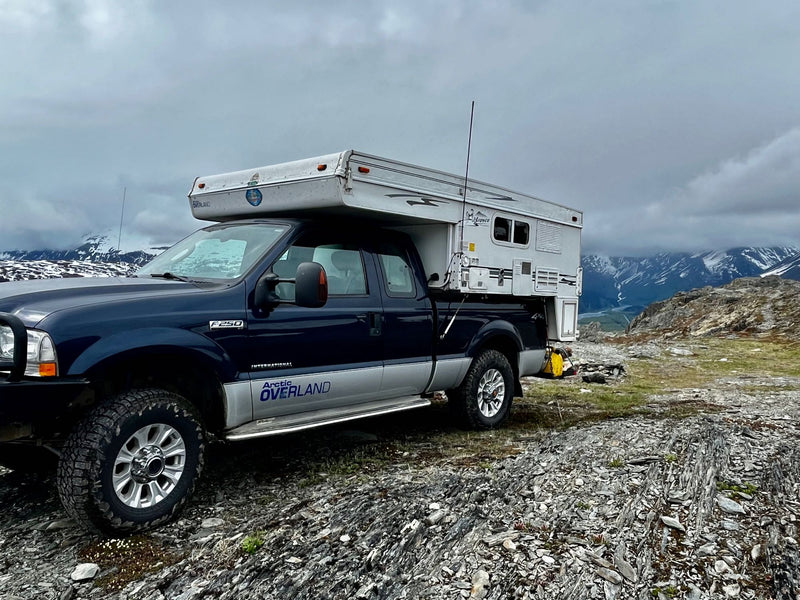  mud-splattered pickup truck with a mounted Bronco truck camper. Ideal for an adventurous RV rental exploring remote landscapes.|A rugged truck camper at the NWT border sign — photo 13