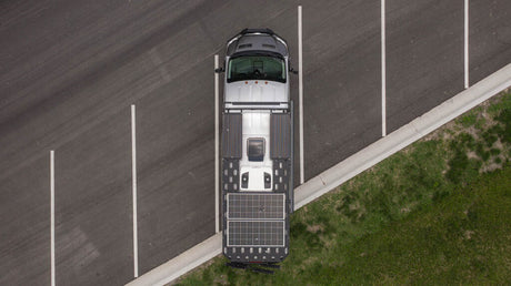 Top-down view of a grey RV rental with rooftop solar panels, parked in a lot. Ideal for off-grid adventures.