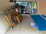 Cozy rv rental van interior with a bed, vibrant pillows, and book for relaxing. Ready for your next adventure!