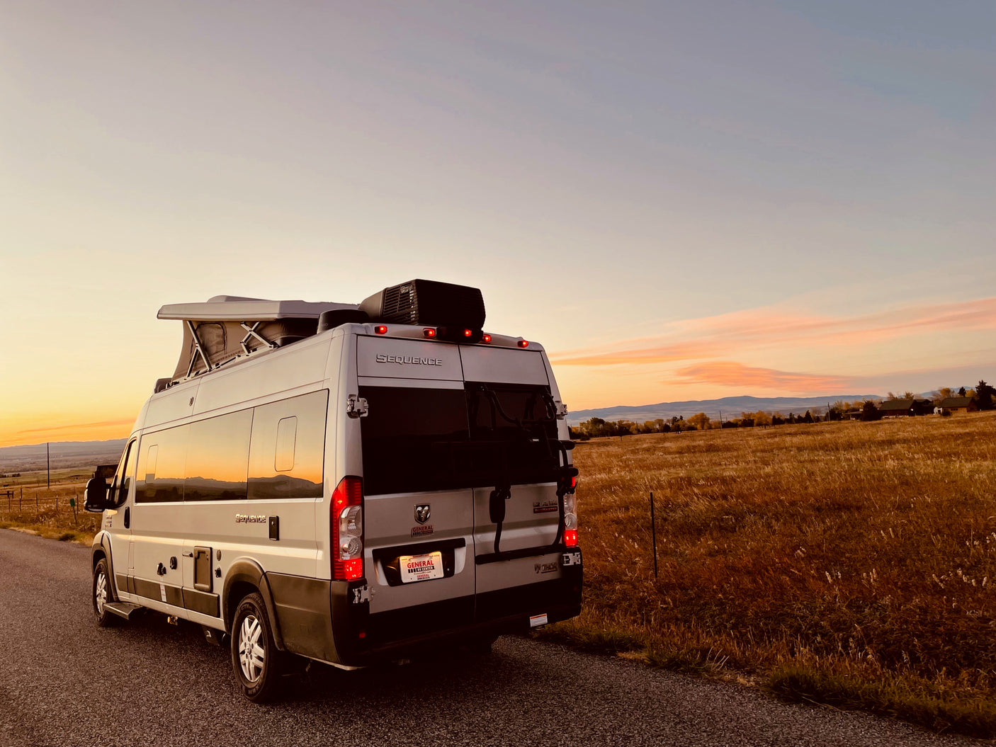 White Thor Sequence camper van rental parked on a rural road at sunset, beside golden fields, pop-top open.