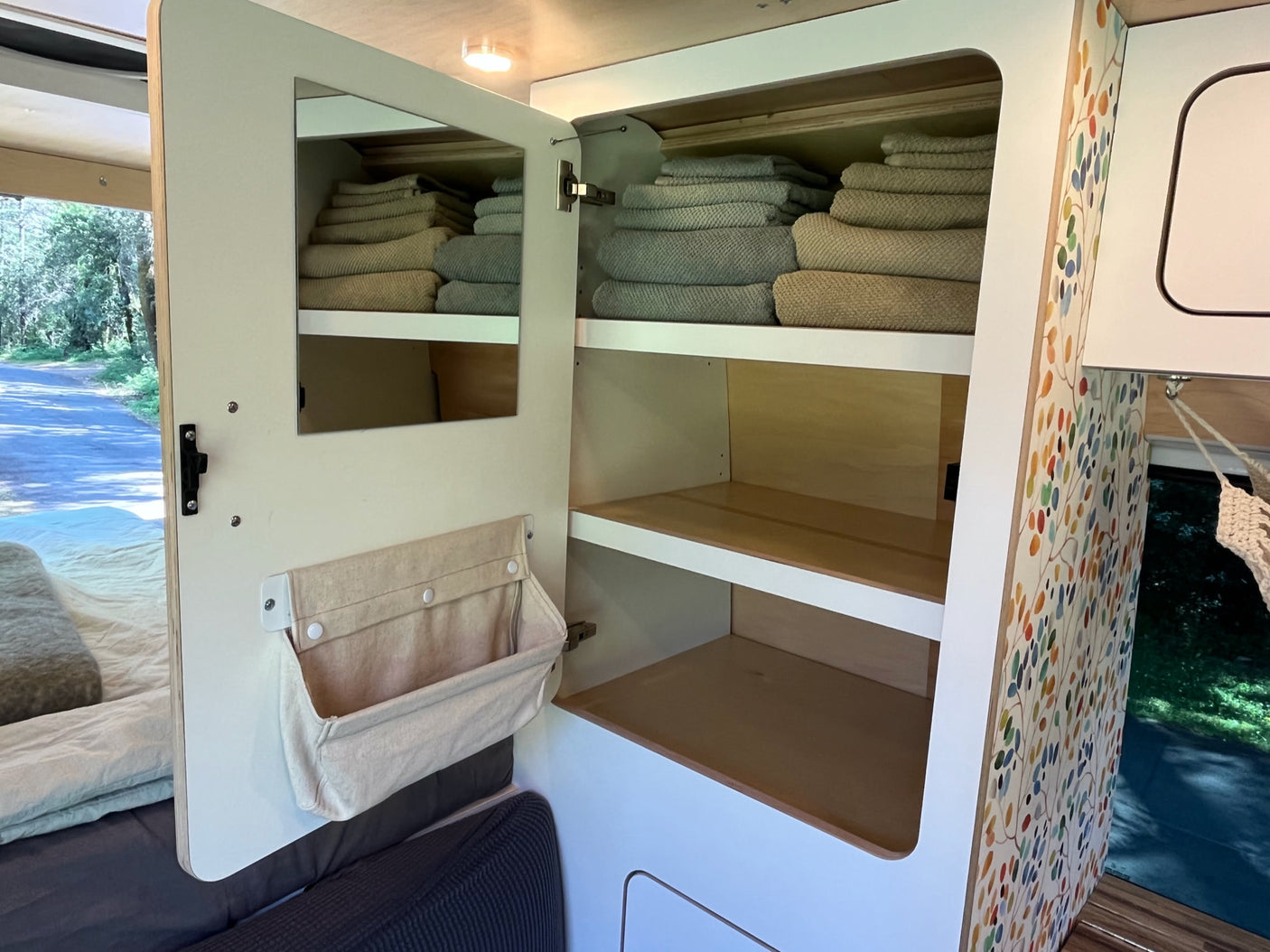RV rental: functional cabinet with mirror door, fabric storage, and shelves of neatly folded towels. Smart camper interior organization.