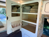 RV rental: functional cabinet with mirror door, fabric storage, and shelves of neatly folded towels. Smart camper interior organization.