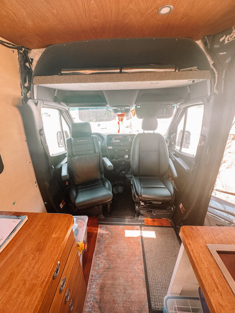Spacious RV rental interior: custom camper van front cabin with black seats, wood ceiling, and cozy conversion.