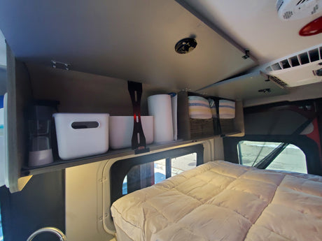 RV rental: Organized overhead shelving with bins & baskets above a cozy bed. Ideal for camper van storage.