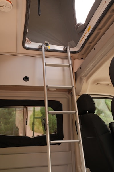  featuring a window view of lush trees and green grass.|Inside an RV rental: a cozy bed with brown bedding — photo 6