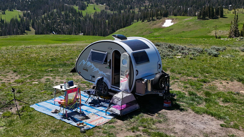Teardrop RV rental set up for off-grid camping in a scenic mountain meadow with pine trees and snow patches. — photo 2