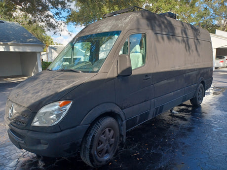 Weathered dark gray Sprinter van on a wet driveway, potentially an rv rental or custom camper van.