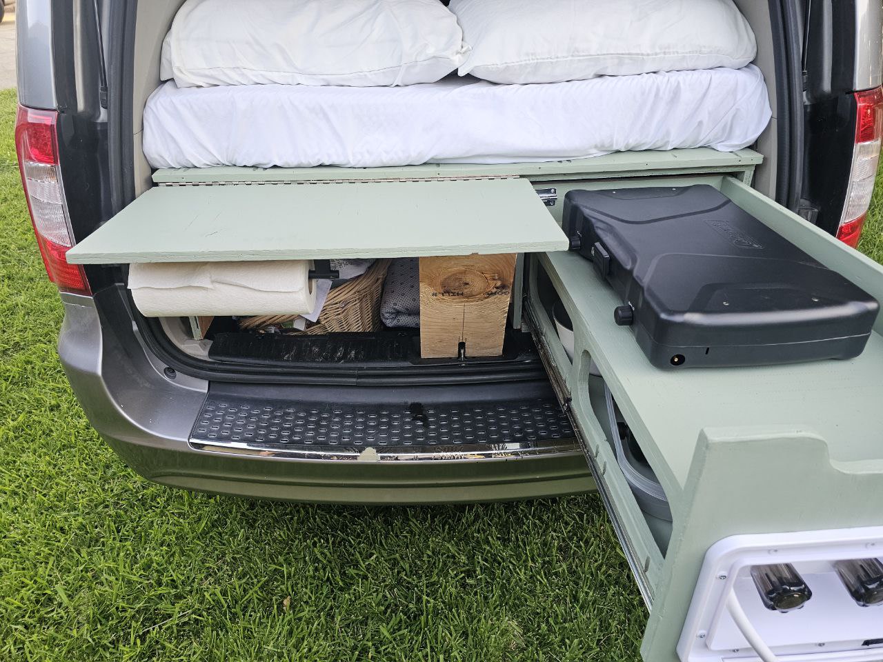 RV rental van conversion: Rear view of open hatch reveals bed, pull-out camping kitchen with stove & water, plus storage. — photo 16