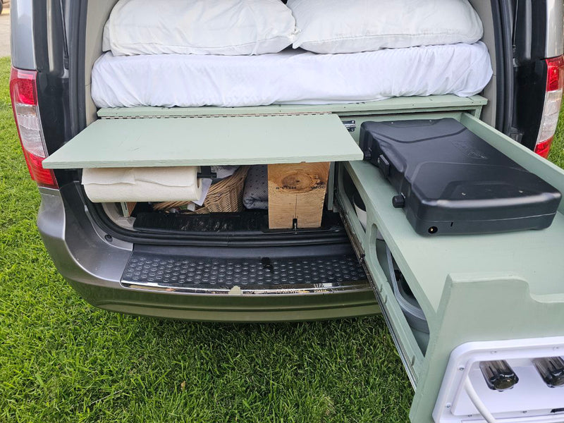 RV rental van conversion: Rear view of open hatch reveals bed, pull-out camping kitchen with stove & water, plus storage. — photo 16