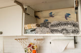 Well-organized kitchen cabinet in an RV rental: folded yellow/white towels, grey cleaning tools, and a manta ray lining.
