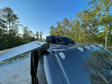 RV rental: An extended awning, rooftop AC, and front marker lights on a camper van, parked amidst trees.