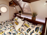 Inside a cozy RV rental: a bed with playful car bedding, a round door, and ambient lighting.