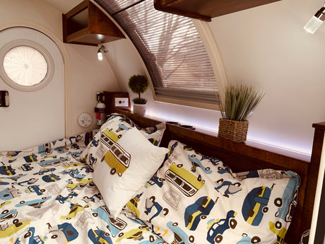 Inside a cozy RV rental: a bed with playful car bedding, a round door, and ambient lighting.