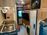 Compact RV rental interior featuring a kitchen with sink/stovetop, microwave, fridge, and cozy living area.