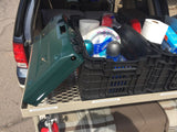 Organized RV rental trunk with pull-out shelf: a green camping stove & crate of Dixie plates/paper towels for cooking & eating.