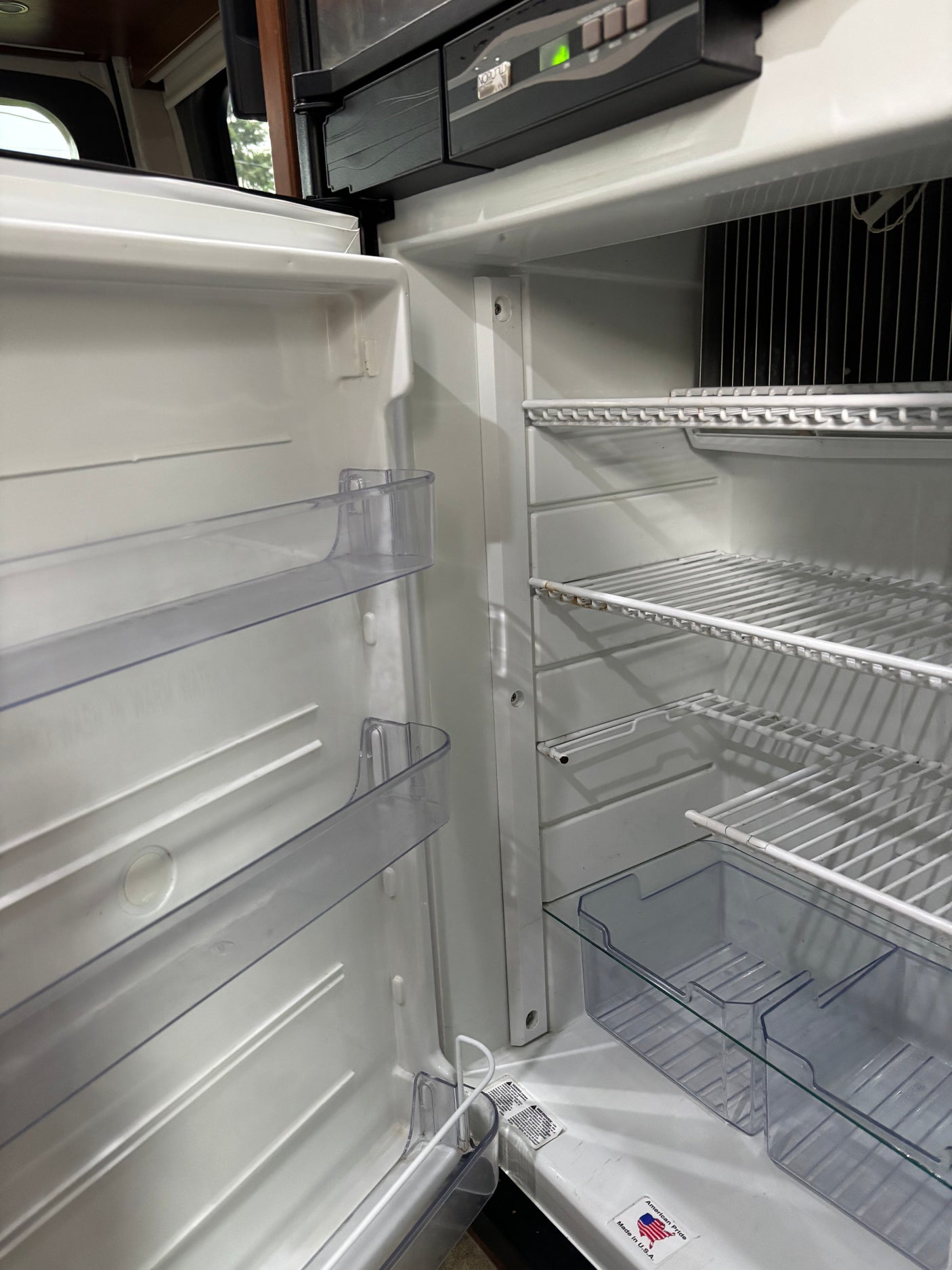 Clean, empty RV rental refrigerator interior, showcasing wire shelves and door bins, ready for your travel provisions.