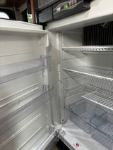 Clean, empty RV rental refrigerator interior, showcasing wire shelves and door bins, ready for your travel provisions.