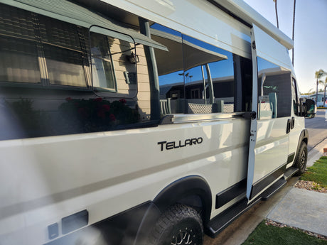 White Tellaro camper van, ideal for rv rental. Side door open, reflections of houses on windows.