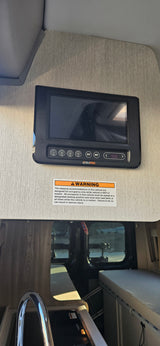 An RV rental's interior, featuring a BMPRO control panel, safety warning, and glimpse of kitchen/sleeping areas.