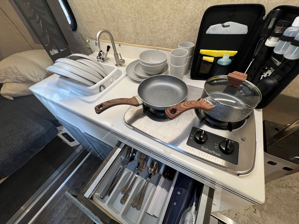This RV rental features a compact, well-equipped kitchen area with a sink, two-burner stove, dishes, and utensils. — photo 12