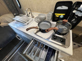 This RV rental features a compact, well-equipped kitchen area with a sink, two-burner stove, dishes, and utensils.