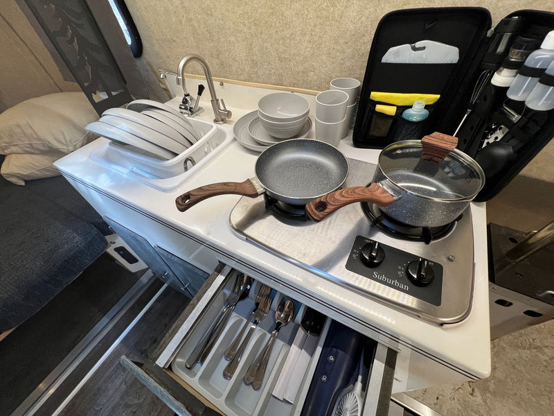 This RV rental features a compact, well-equipped kitchen area with a sink, two-burner stove, dishes, and utensils. — photo 12