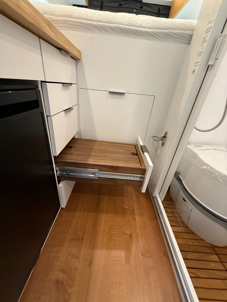 Functional RV rental interior: compact kitchen/storage with pull-out table, cozy bed above, and compact bathroom.
