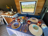 A cozy RV rental interior with a table set for a meal, featuring fruit, cheese, wine, and a scenic vineyard view outside.