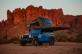 Off-road RV rental: Blue Jeep with rooftop tent & awning in stunning red rock desert for adventure camping.