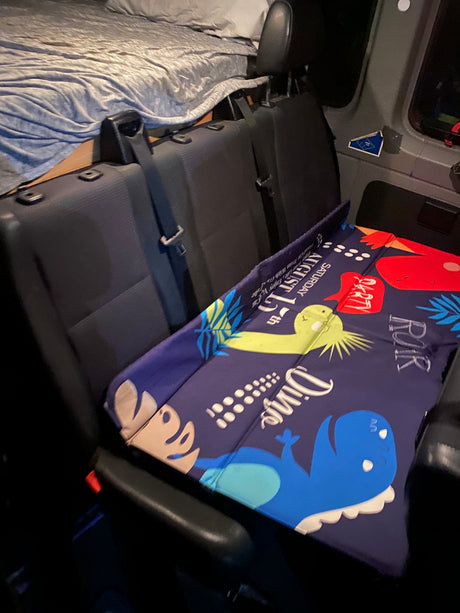 RV rental camper van interior featuring a cozy bed, passenger seats, and a fun dinosaur mat for kids.