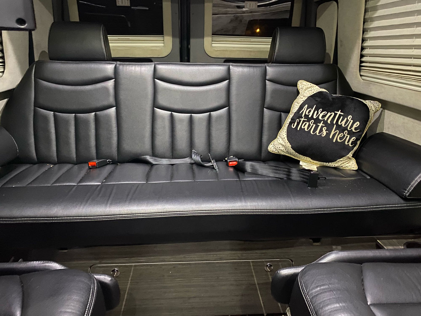 Spacious RV rental interior: black leather bench seat with seatbelts & an "Adventure starts here" pillow.