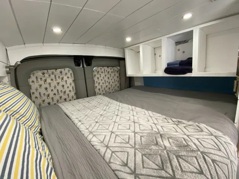 Cozy RV rental bedroom with a comfy bed, overhead storage, and fun cactus window covers. — photo 9