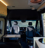 Inside a modern rv rental van: front seats, a pull-out table on the left, and a kitchen counter with stovetop on the right.