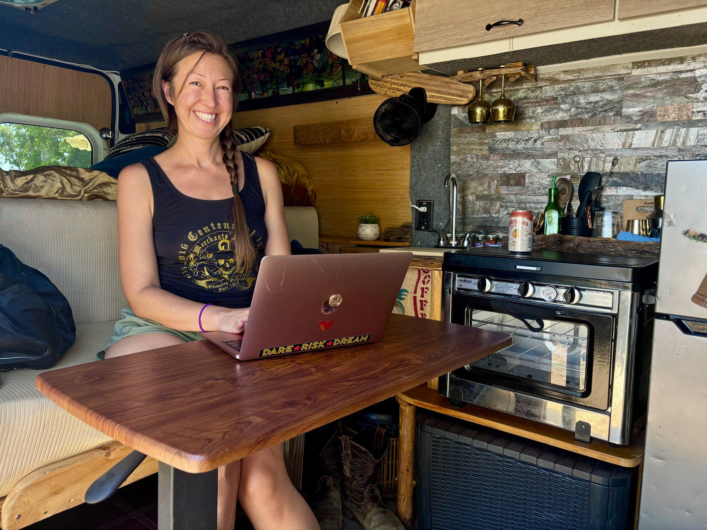A smiling woman works on her laptop at a desk inside a well-equipped RV rental, showcasing compact mobile living.
