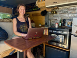 A smiling woman works on her laptop at a desk inside a well-equipped RV rental, showcasing compact mobile living.