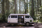 A white camper van, ideal for RV rental adventures, parked in a sunny forest with its side door open.