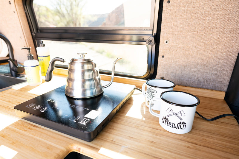 RV rental kitchen: Kettle on induction cooktop, Mrs. Meyer's soaps, & 'Staywild' mugs on wood counter. Ready for adventure. — photo 12